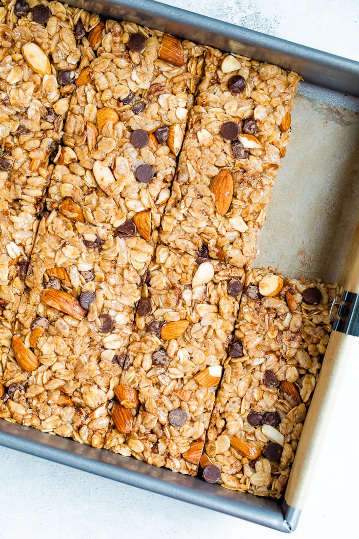 Metallpfanne mit Schokoladenchip-Mandel-Granola-Riegeln in Riegel schneiden.