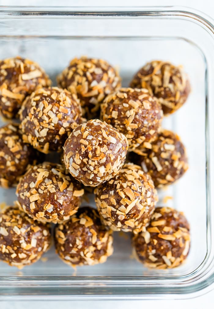 Energy balls coated in toasted coconut in a glass storage container.