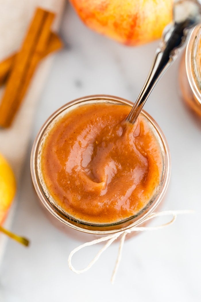 Bird's eye view of a jar with a spoon and filled with apple butter. The jar has a twine bow tied around it.