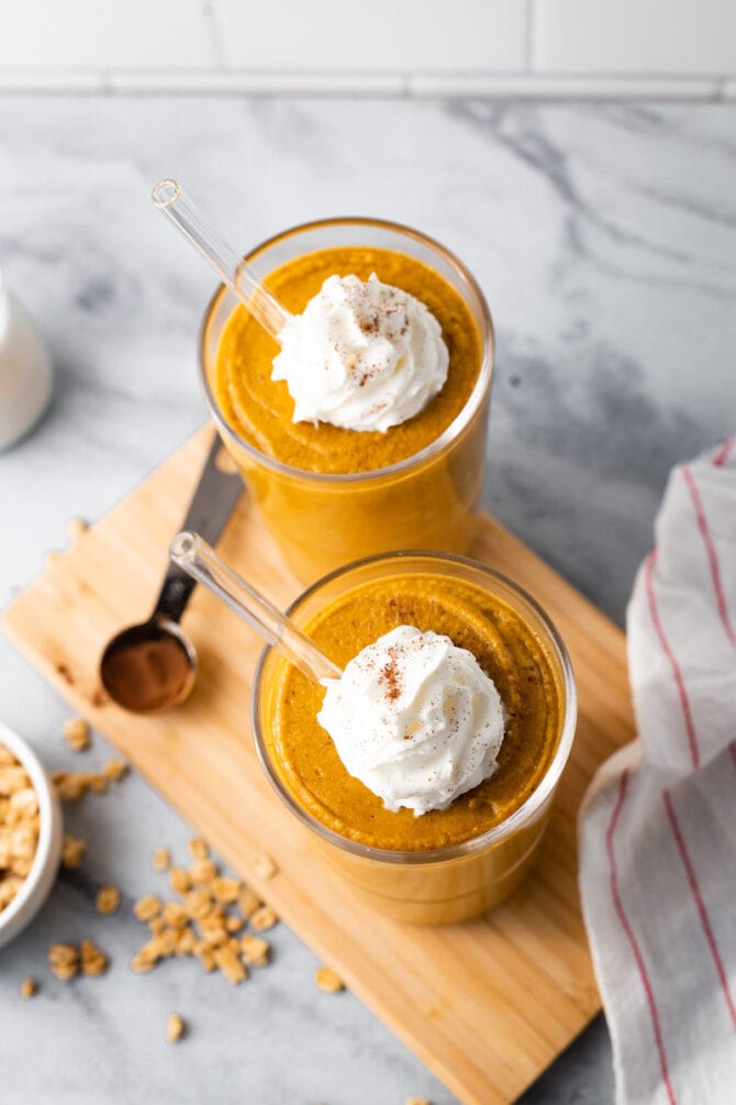 Two glasses of pumpkin pie smoothies topped with whipped cream and pumpkin spice.