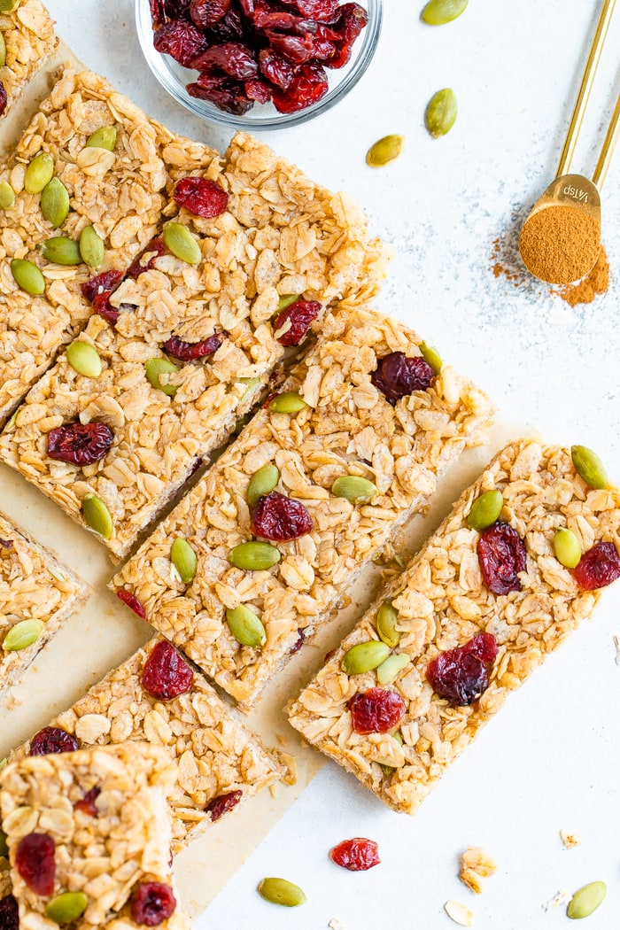 Pumpkin spice granola bars next to a bowl of dried cranberries and teaspoon with cinnamon.