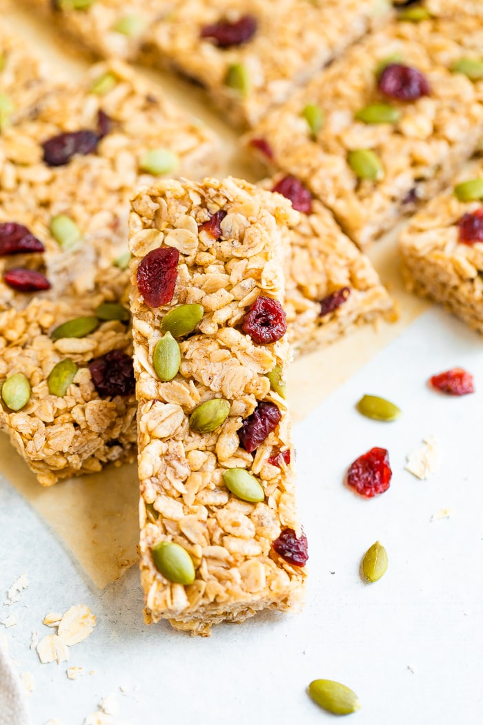 Pumpkin spice granola bars with cranberries and pepitas stacked on a table.