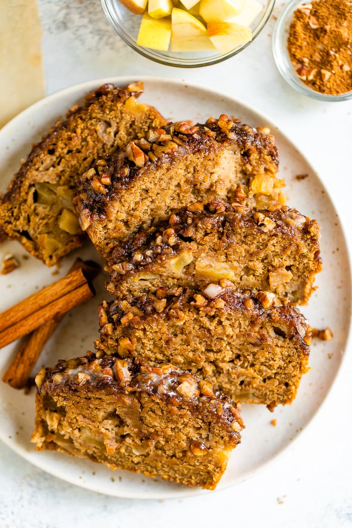 Plate with 5 slices of apple bread with a cinnamon pecan crust. Two cinnamon sticks are on the plate.