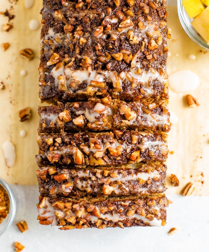 Overhead photo of a loaf of apple bread sliced up and topped with cinnamon sugar, pecans and a glaze.