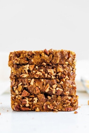 Stack of four slices of apple bread topped with cinnamon sugar and pecans.