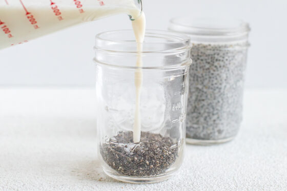 Pouring almond milk into a mason jar with chia seeds to make chia pudding.