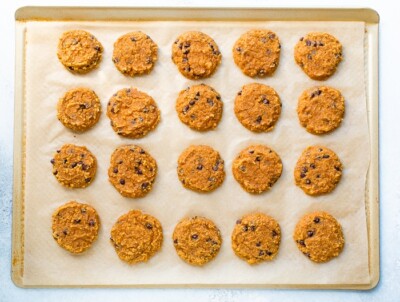 20 cooked pumpkin cookies on a gold baking sheet lined with parchment.