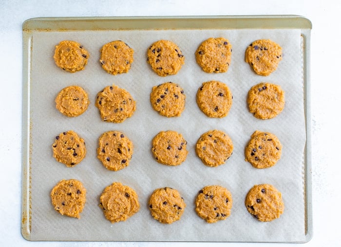 20 unbaked pumpkin cookies on a gold baking sheet lined with parchment.