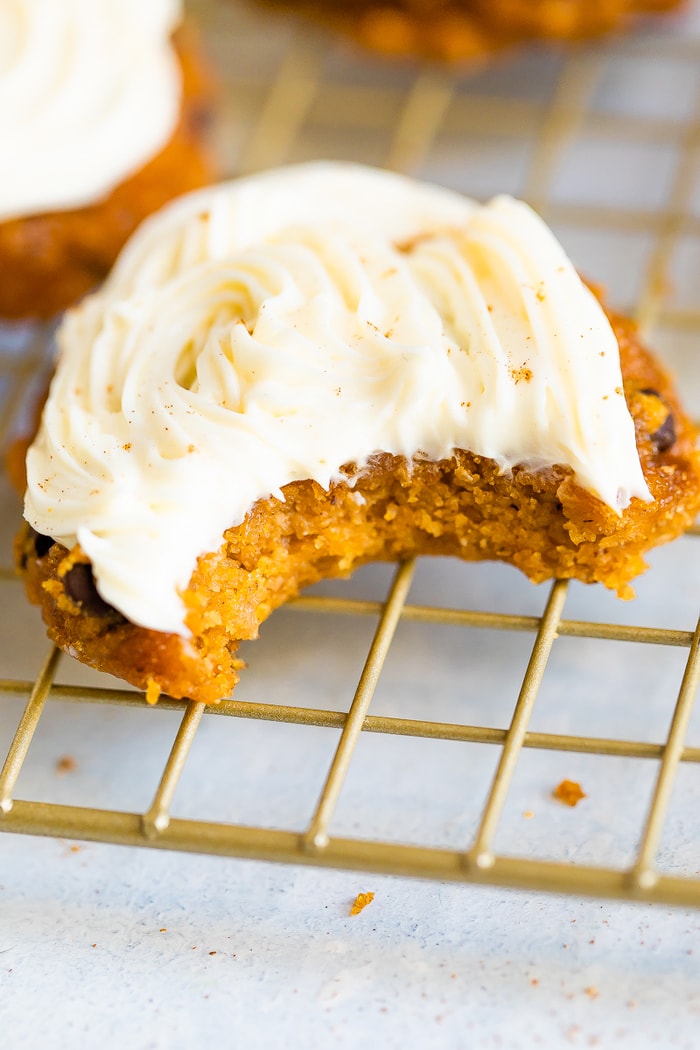 Pumpkin cookie topped with icing and a bite is taken out of it.