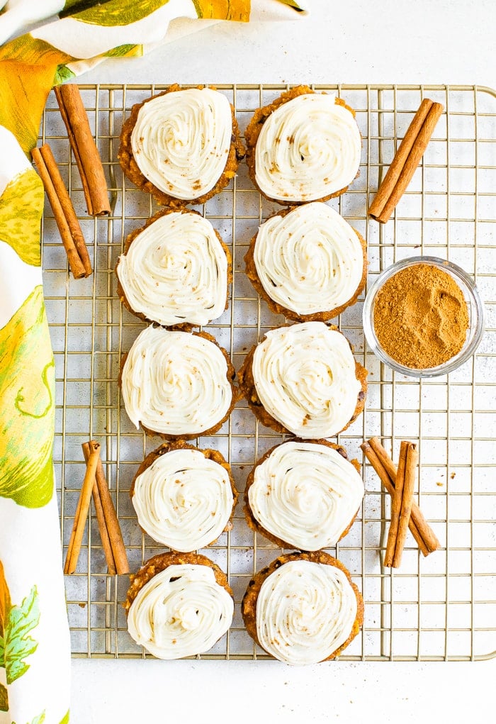 Iced pumpkin cookies on a cooling rack with cinnamon sticks.