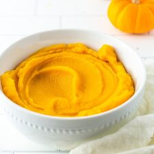 Bowl with pumpkin puree. A cloth and mini pumpkins are on the table around the bowl.