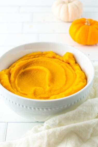 Bowl with pumpkin puree. A cloth and mini pumpkins are on the table around the bowl.