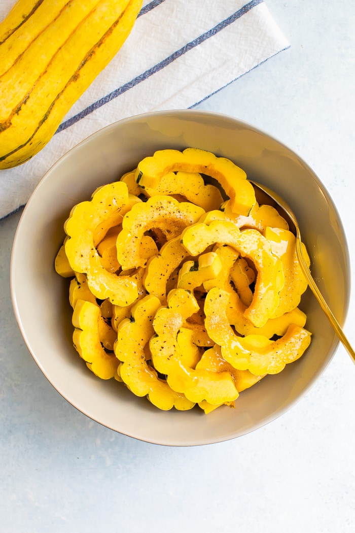Delicata squash in a bowl drizzled with olive oil and pepper.