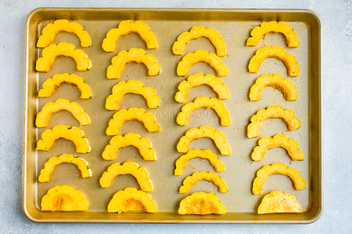 Rings of delicata squash cut in half and lined up on a baking sheet.