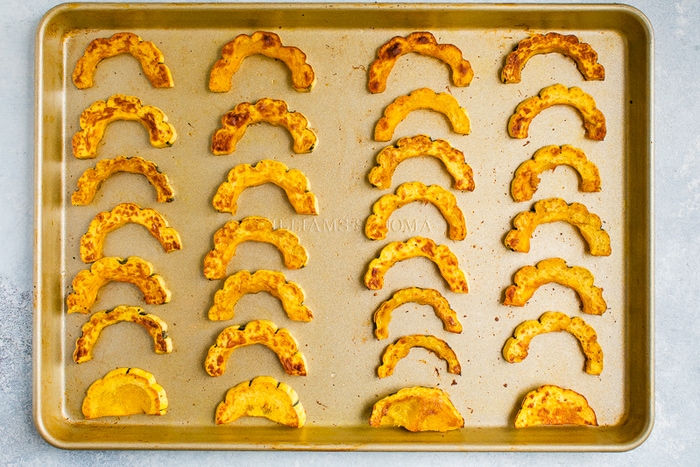 Half circles of delicata squash roasted on a sheet pan.