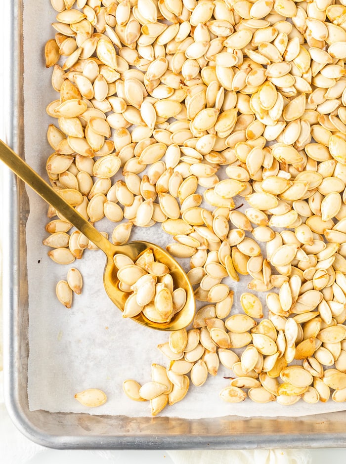 Roasted pumpkin seeds on a baking sheet with a spoon.