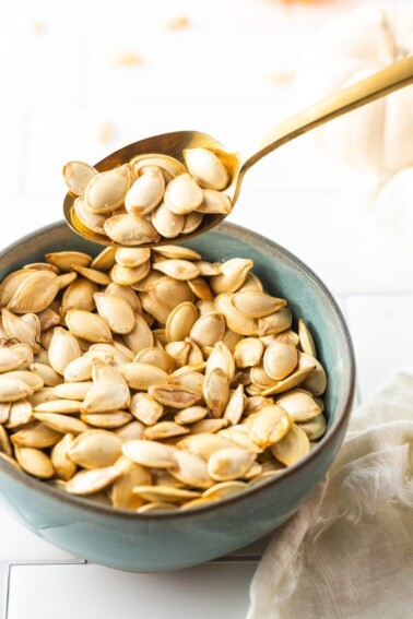 Spoon scooping up some roasted pumpkin seeds from a bowl.