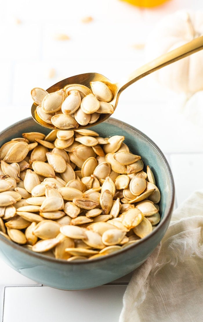 Spoon scooping up some roasted pumpkin seeds from a bowl.