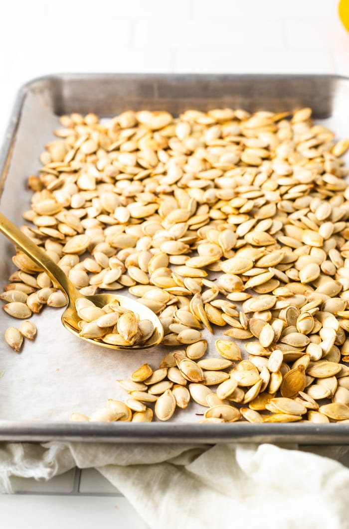 Roasted pumpkin seeds on a baking sheet with a spoon.