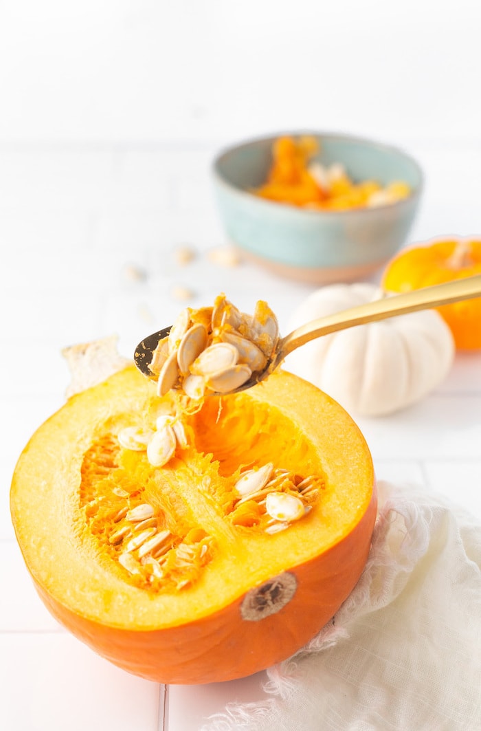 Spoon scooping seeds out of half a pumpkin.