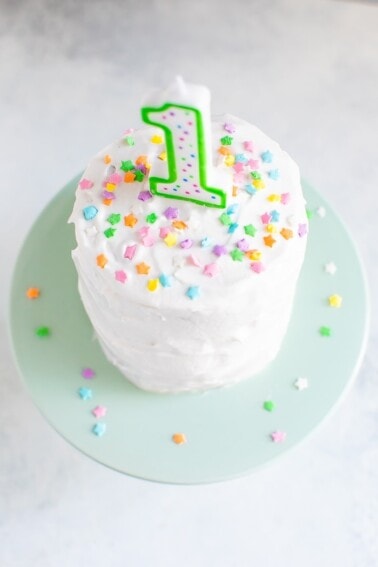 Small smash cake with white frosting, a "1" birthday candle and colorful star sprinkles.