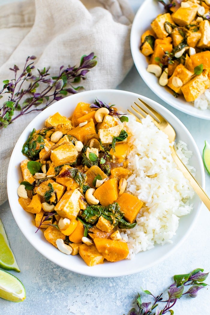 Bowls of tofu pumpkin curry topped with cashews and served with rice.