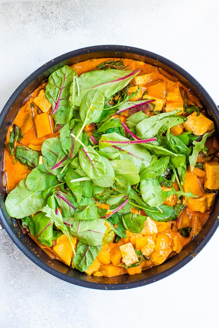 Pot of tofu pumpkin curry with fresh greens.