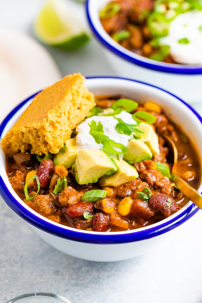 Bowl of turkey chili with sour cream, avocado and cornbread.