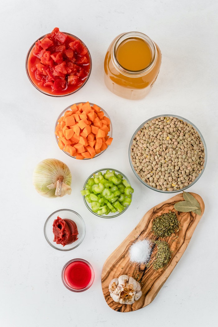 Ingredients to make lentil soup including tomatoes, broth, carrots, lentils, onion, celery, tomato paste, garlic, vinegar and spices.