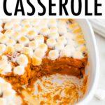 Sweet potato casserole topped with marshmallows. A spoon is in the casserole scooping a portion out.
