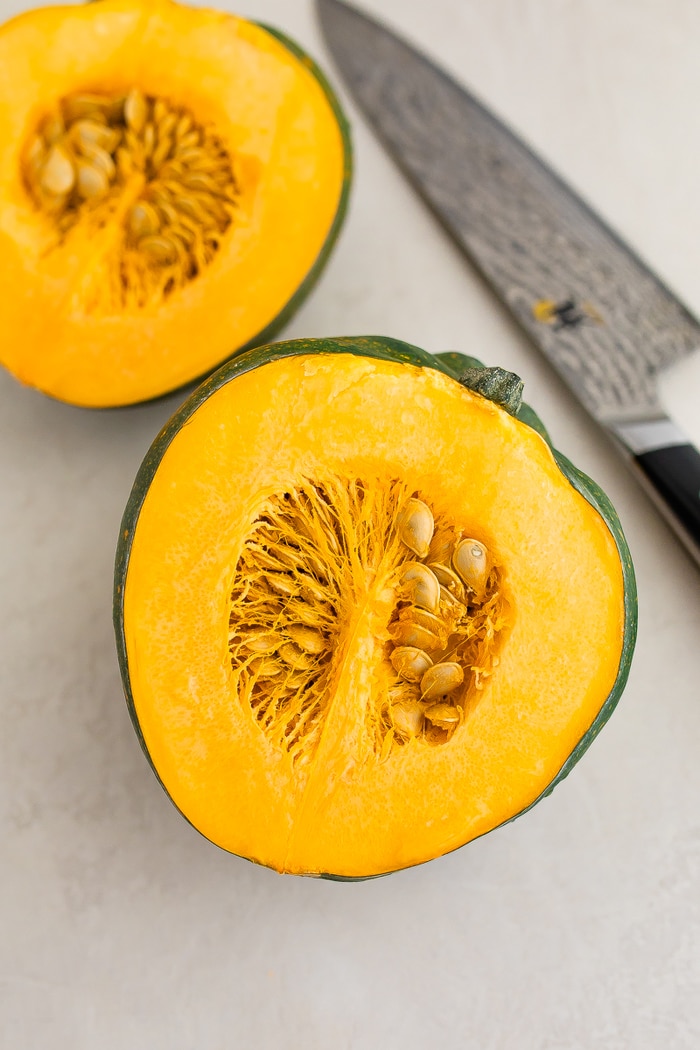 Acorn squash sliced in half. A knife is beside the squash.