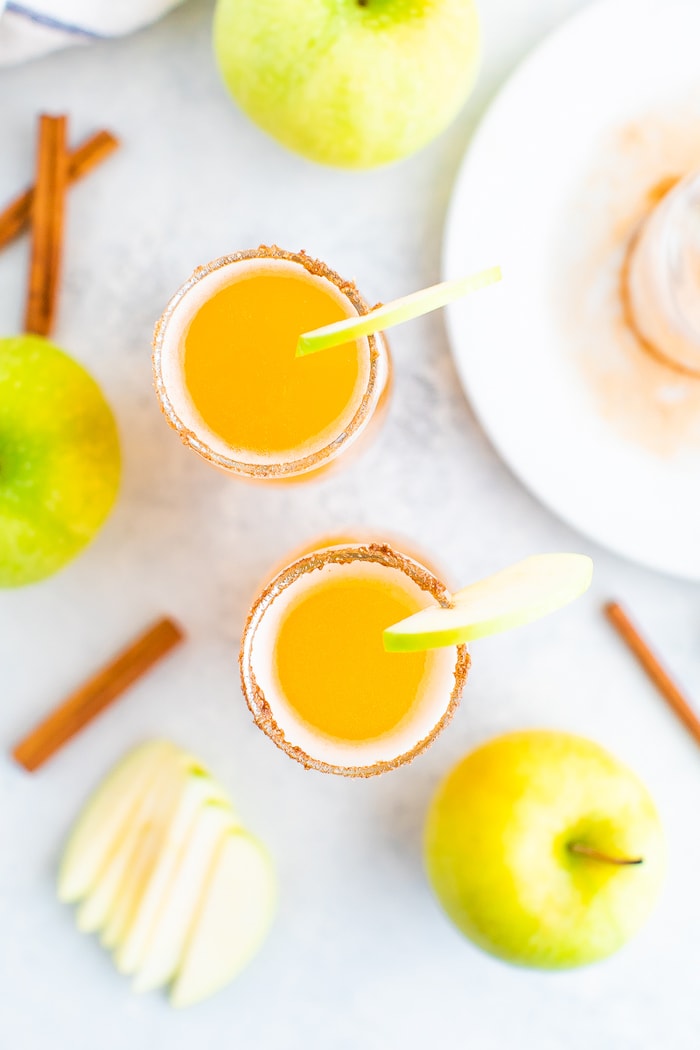 Bird's eye view of two apple cider mimosa glasses garnished with a cinnamon rim and apple slice.