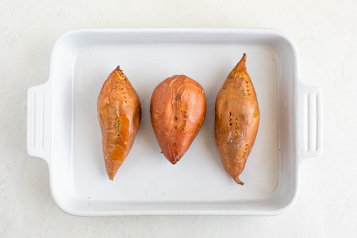 Three baked sweet potatoes in a baking dish.