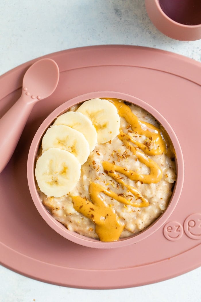 Rolled oats for baby with banana, peanut butter and flaxseed in a ezpz bowl with an ezpz spoon on the side.