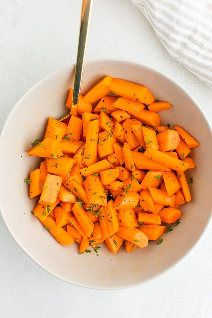 A mixing bowl with chopped carrots tossed with herbs, salt and pepper and oil.