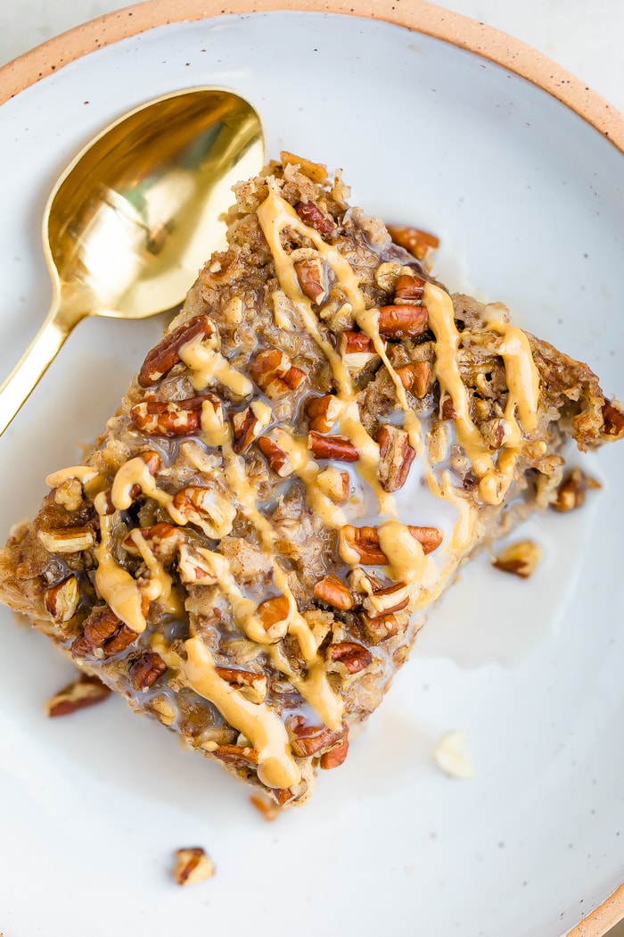 A piece of maple pecan baked oatmeal, topped with peanut butter and almond milk in a bowl with a gold spoon.