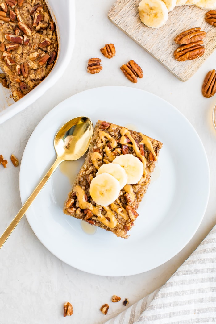 Slice of maple pecan baked oatmeal on a plate topped with peanut butter and banana slices.