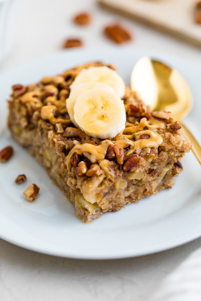 Slice of maple pecan baked oatmeal on a plate topped with peanut butter and banana slices.