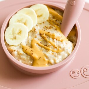 Rolled oats for baby with banana, peanut butter and flaxseed in a ezpz bowl with an ezpz spoon in the oatmeal.