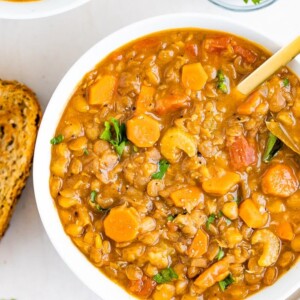 Bowl of lentil soup with celery and carrots. Beside the bowl is a slice of bread and parsley.