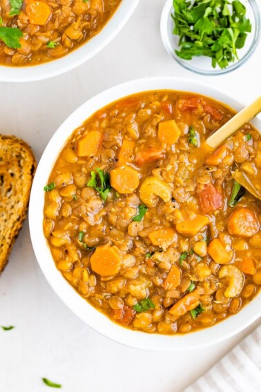 Bowl of lentil soup with celery and carrots. Beside the bowl is a slice of bread and parsley.