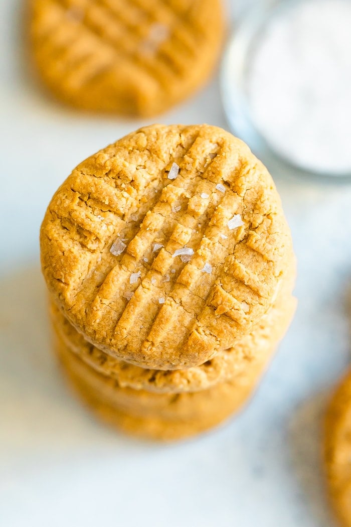 Peanut butter cookies in a stack. Sea salt is sprinkled on top of the cookie.