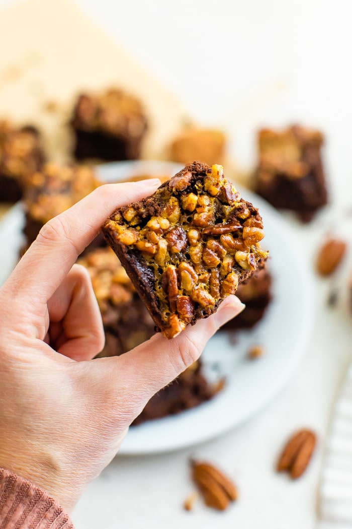 Hand holding a brownie topped with pecan pie topping.