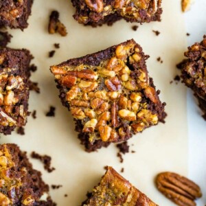 Pecan pie brownies on a table surrounded by pecans.