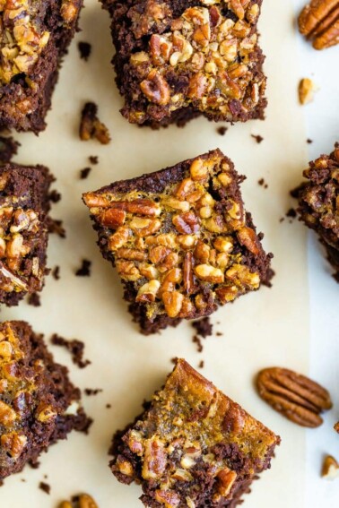Pecan pie brownies on a table surrounded by pecans.