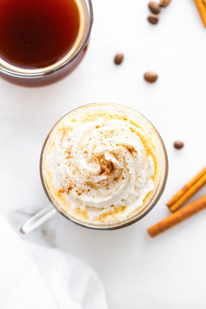Overhead photo of a glass mug full of a pumpkin spice latter topped with whipped cream and pumpkin spice.