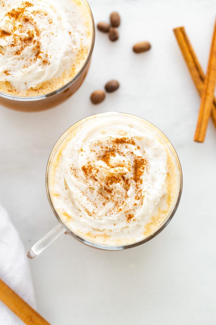 Overhead photo of two glass mugs of pumpkin spice lattes topped with whipped cream and a sprinkle of pumpkin spice.