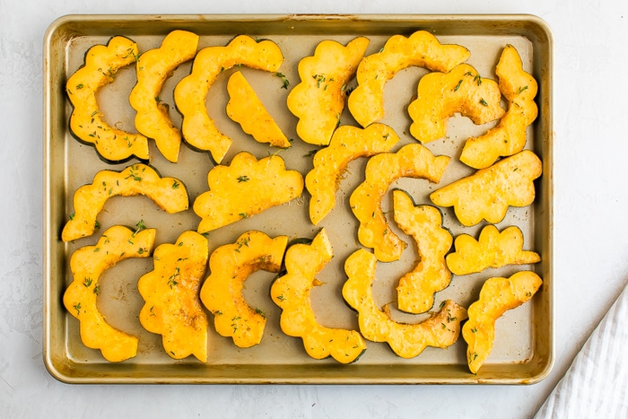 Half circle slices of acorn squash uncooked on a cookie sheet.