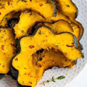 Slices of roasted acorn squash on a plate and seasoned with spices.