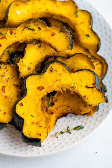 Slices of roasted acorn squash on a plate and seasoned with spices.